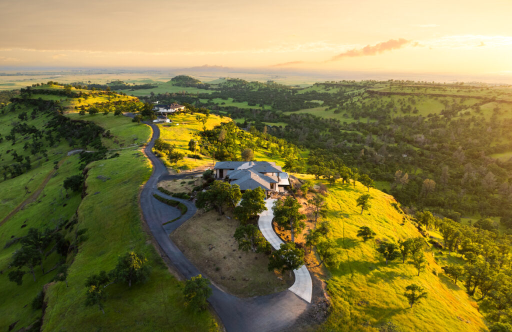 Aerial view of a modern luxury residence in Butte County with sweeping golden hills at sunset.