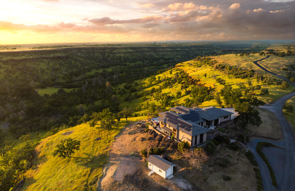 Hilltop custom home in Butte County surrounded by green rolling hills and dramatic sky